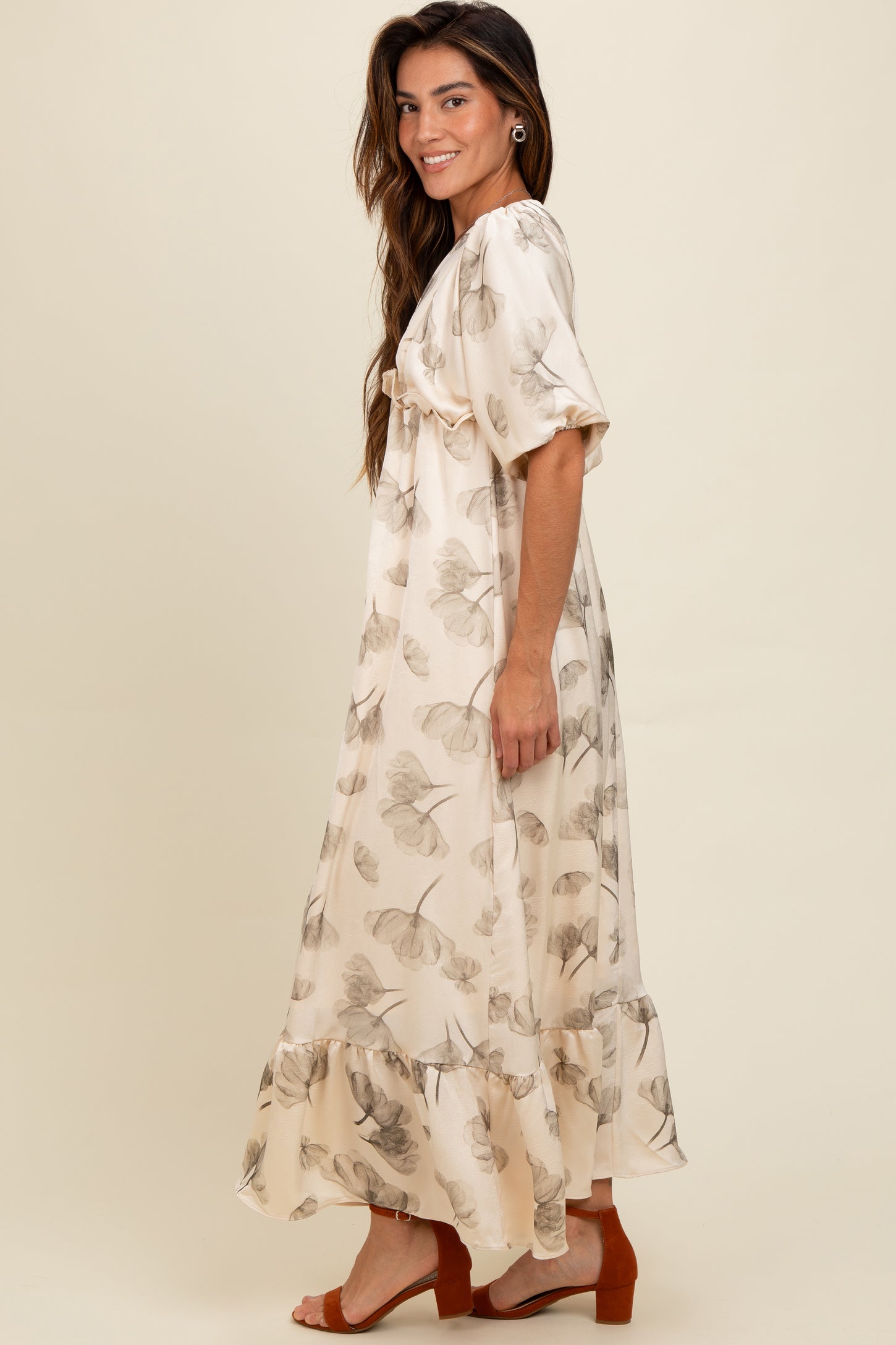 woman wearing a cream floral maxi dress with ruffle hem and short sleeves, standing sideways against a neutral background