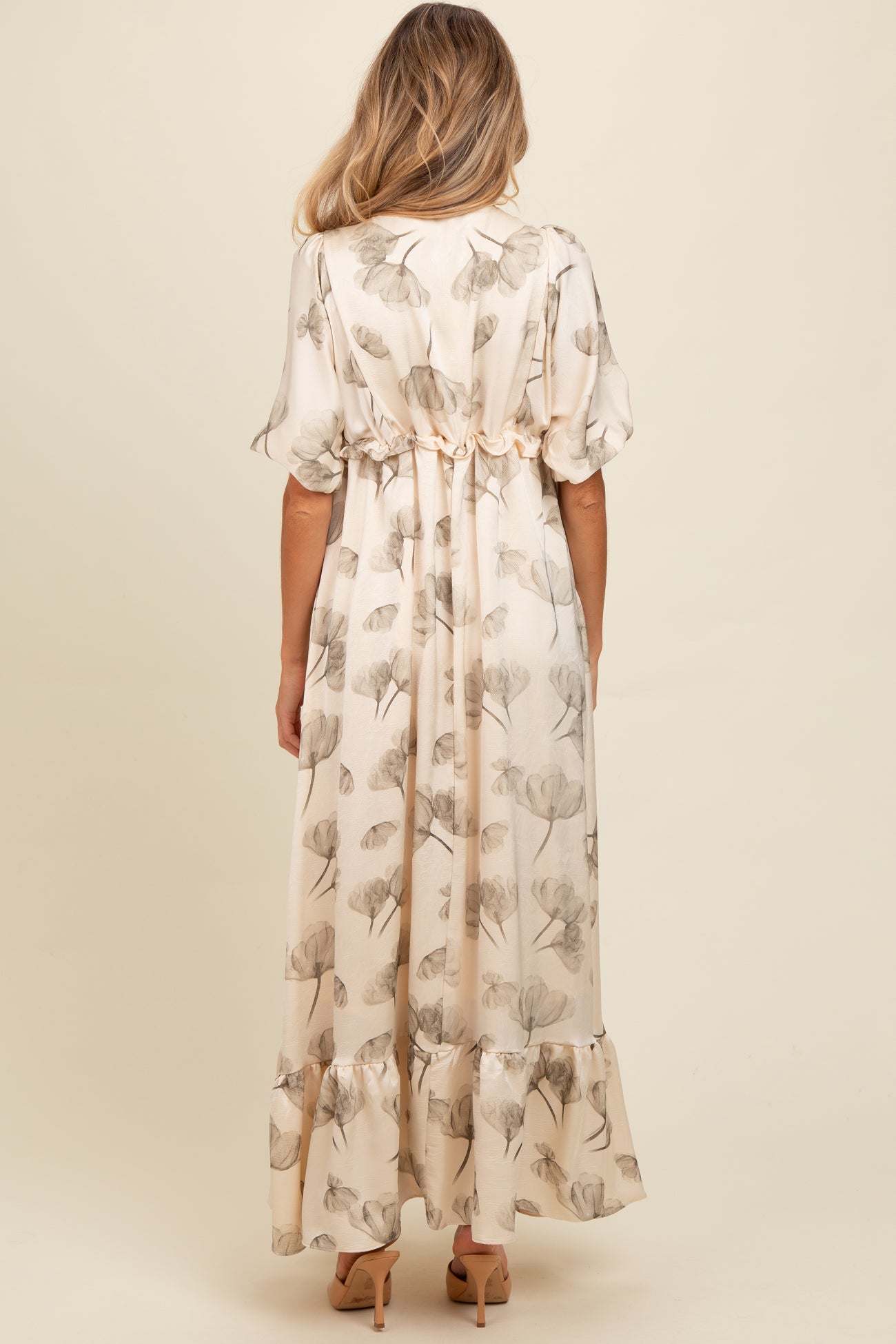 woman wearing a cream floral print maternity maxi dress with a ruffled hem and gathered waist from the back