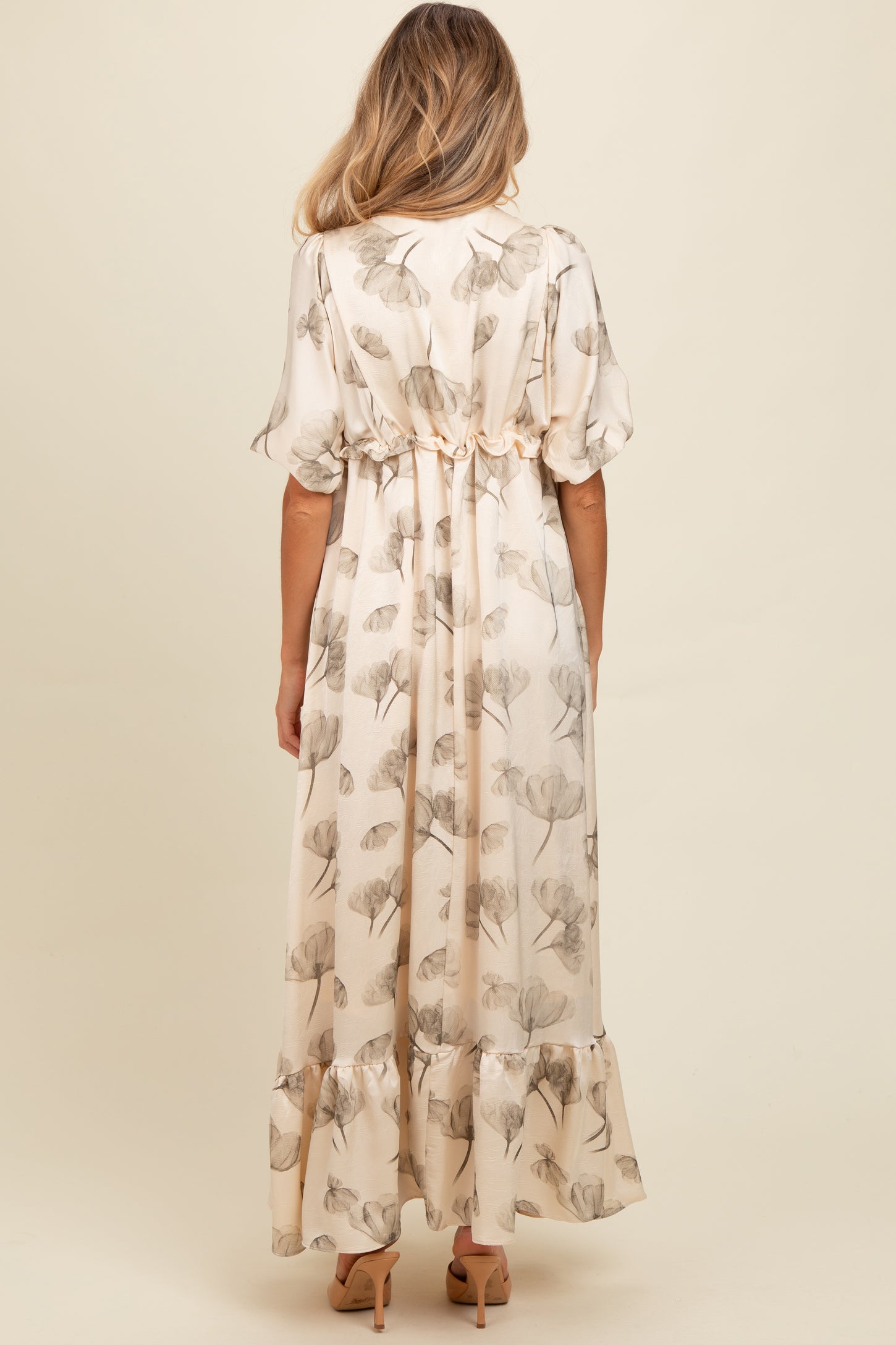 woman wearing a cream floral print maternity maxi dress with a ruffled hem and gathered waist from the back