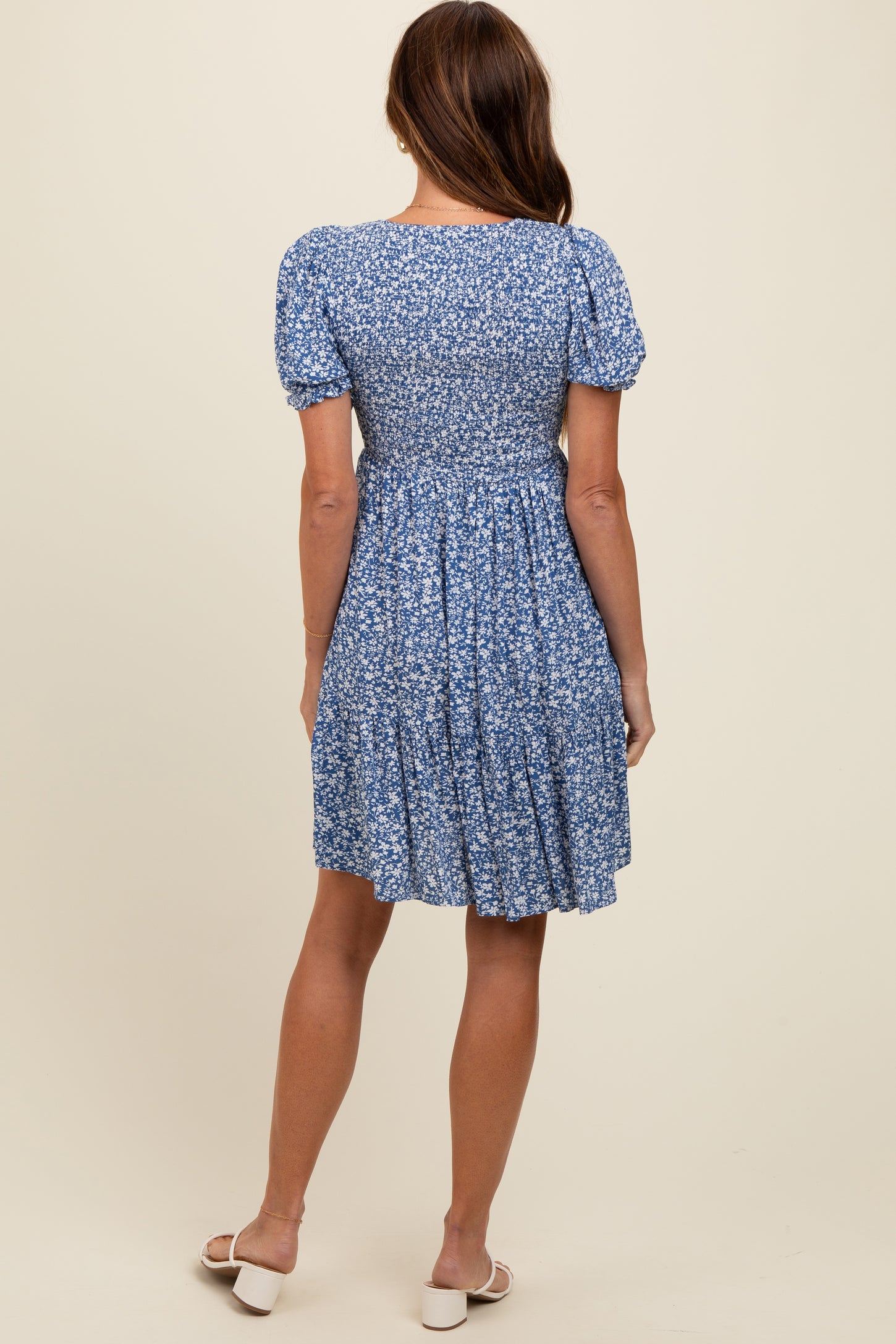 woman wearing a short-sleeve blue floral dress with a smocked bodice and a tiered skirt, shown from the back
