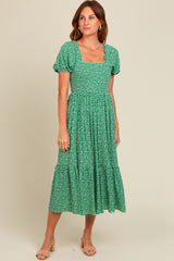 woman wearing a green floral midi dress with puff sleeves and a square neckline, standing against a light background