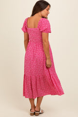 woman wearing a pink floral maternity dress with short puff sleeves and a tiered skirt, showing her baby bump