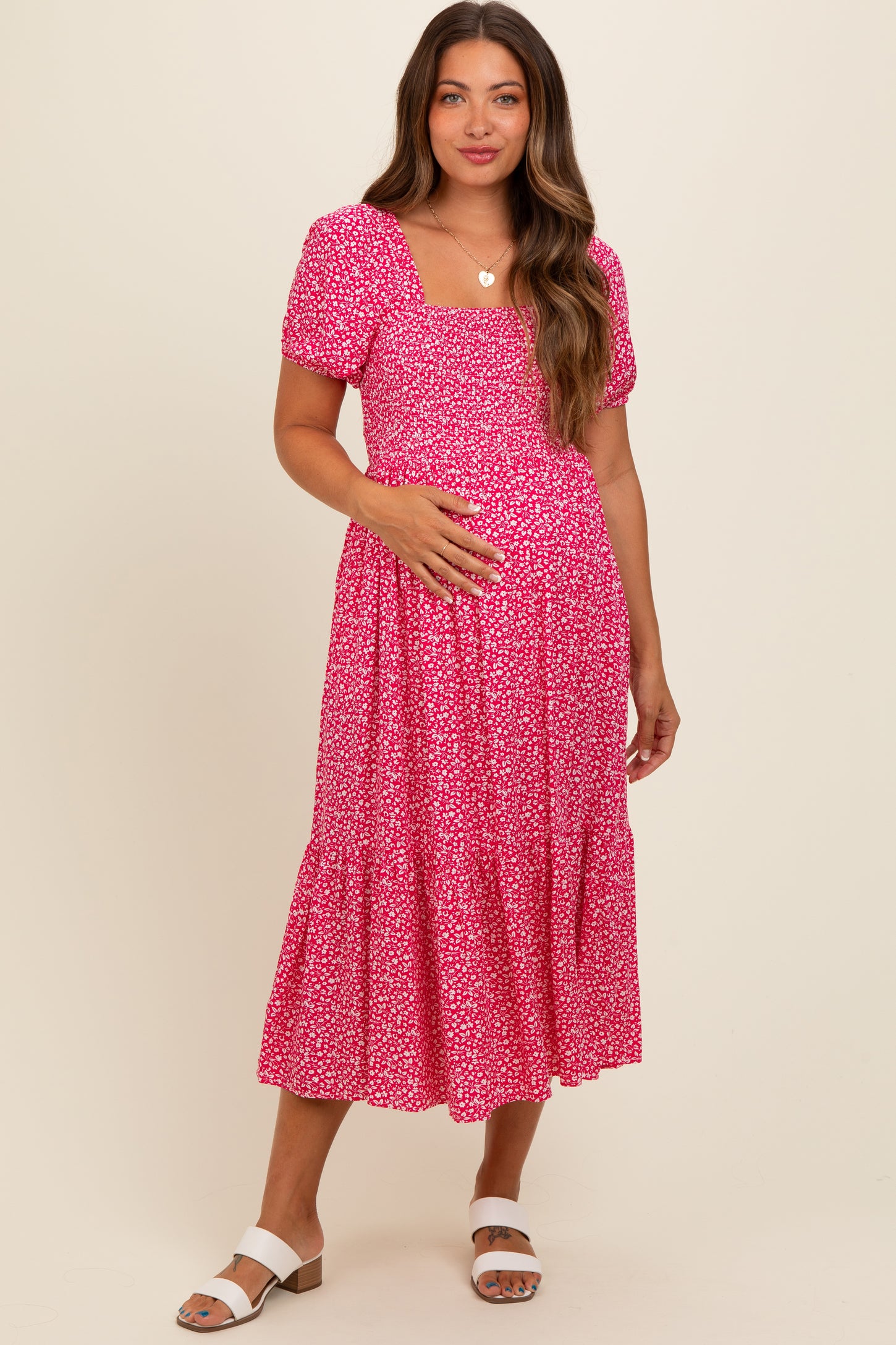 woman wearing a pink floral maternity dress with puff sleeves and a tiered skirt, holding her baby bump