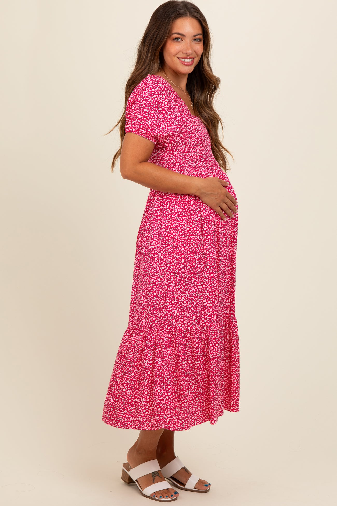 woman wearing a pink floral maternity dress with short sleeves and a tiered hem, holding her baby bump