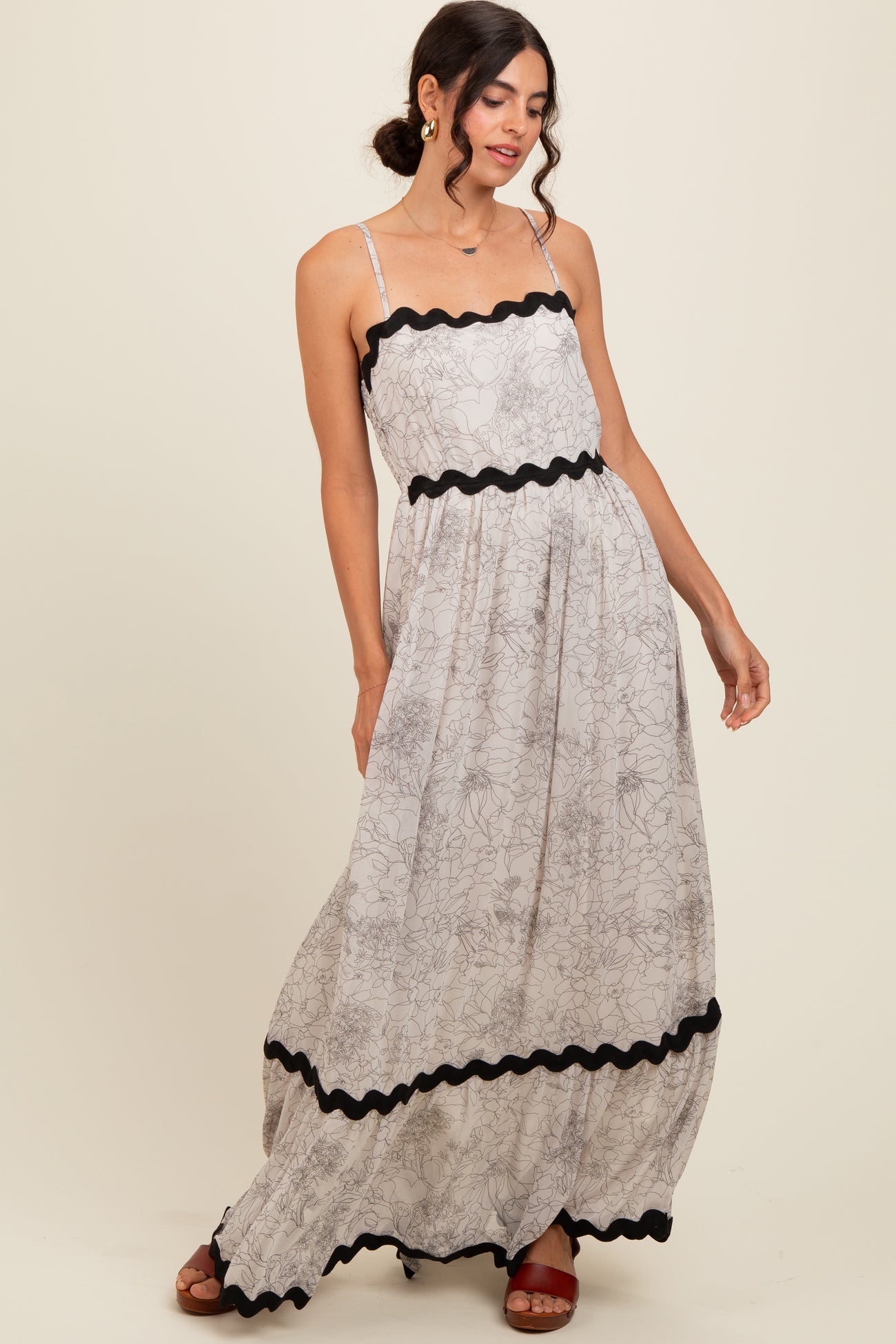 woman wearing a floral print maxi dress with black trim and spaghetti straps, posed with one hand on her hip