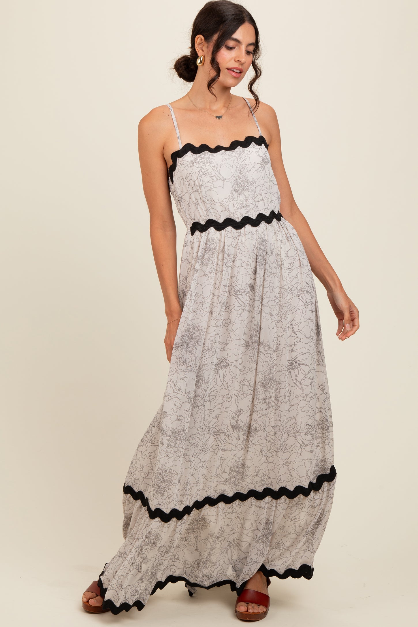 woman wearing a floral print maxi dress with black trim and spaghetti straps, posed with one hand on her hip