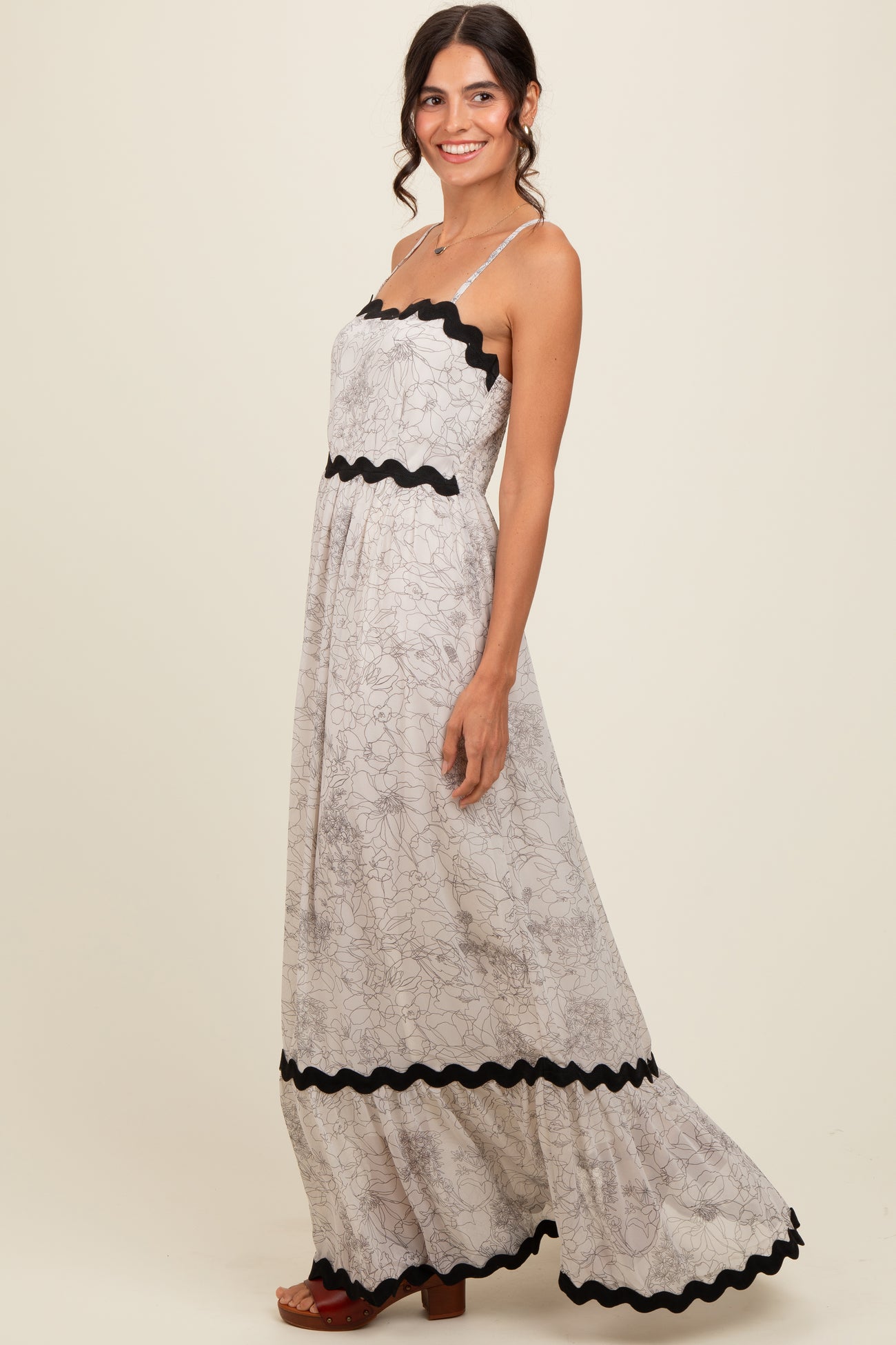 woman wearing a floral maxi dress with black scalloped trim and spaghetti straps, styled with brown heeled sandals