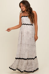 woman wearing a light beige floral maternity maxi dress with black trim and spaghetti straps, showing her baby bump