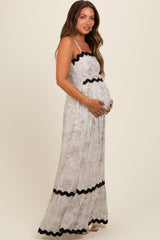 woman wearing a floral maternity maxi dress with black scalloped trim and holding her baby bump