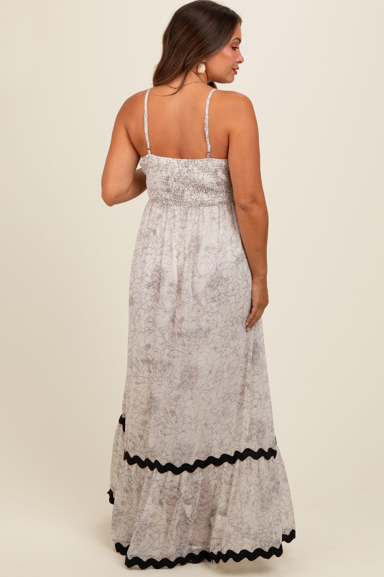 woman wearing a light floral maternity maxi dress with smocked bodice and black ruffle details on the hem