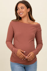 woman wearing a terracotta off-shoulder maternity top with ruching, showcasing her baby bump in denim jeans
