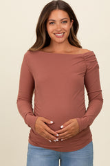 woman wearing a rust long sleeve maternity top with off-shoulder design and holding her baby bump