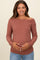 woman wearing a rust long sleeve maternity top with off-shoulder design and holding her baby bump