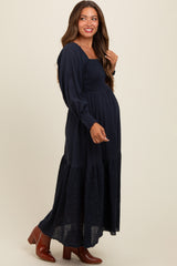 woman wearing a navy blue maternity maxi dress with a smocked bodice and embroidered hem, showing her baby bump