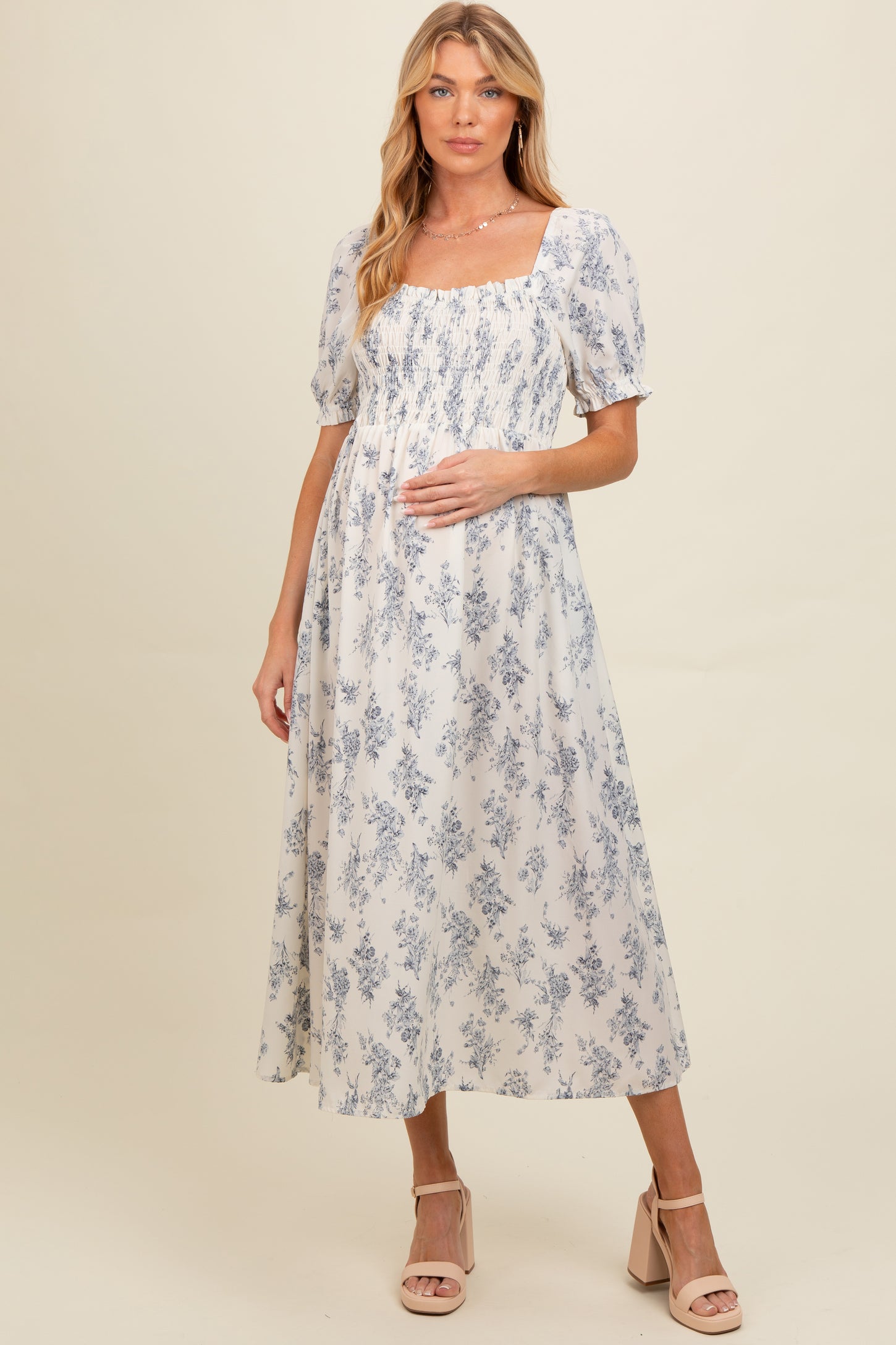 woman wearing a floral print maternity dress with puff sleeves and a smocked bodice, holding her baby bump