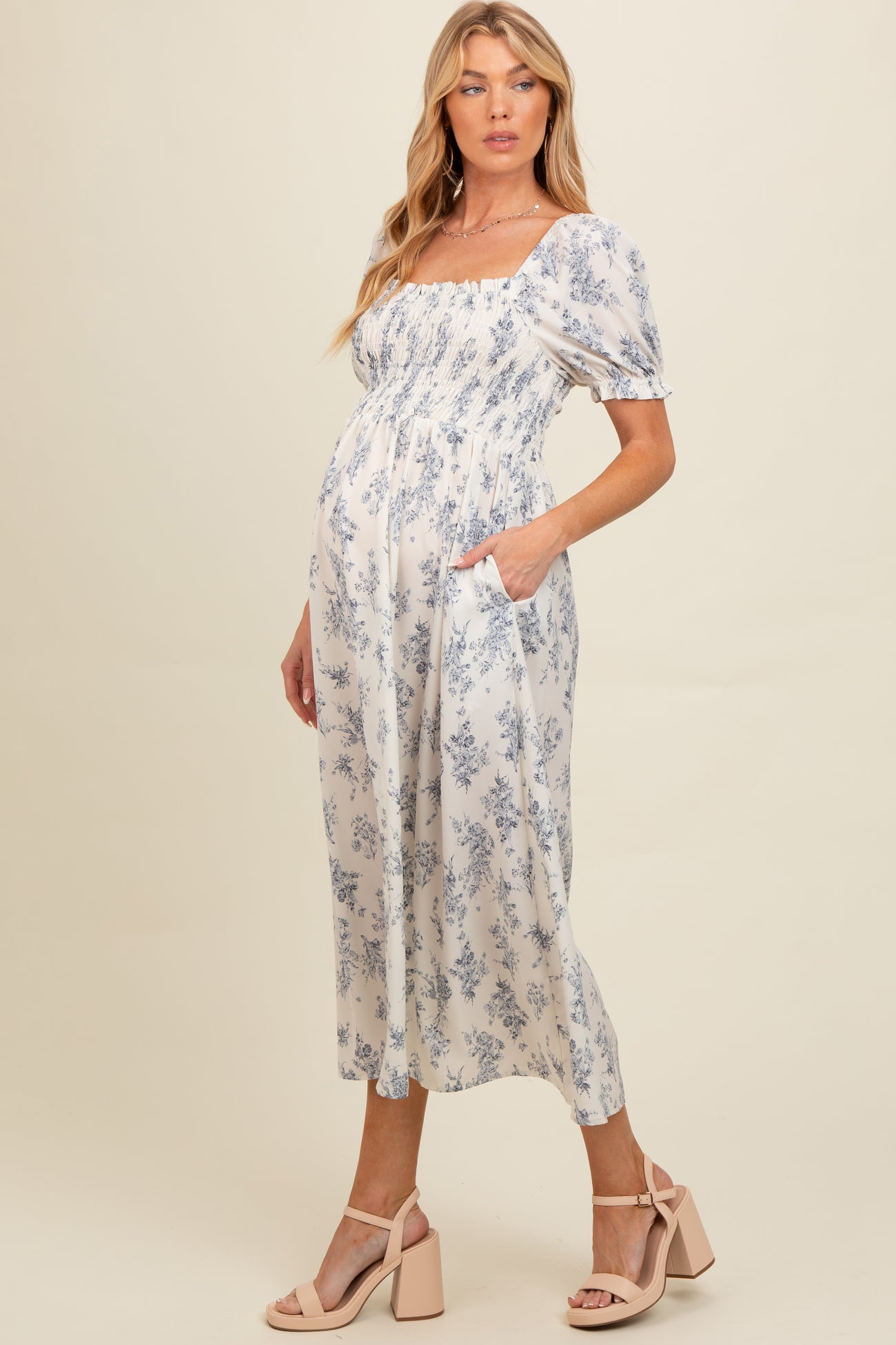 woman wearing a light blue floral maternity dress with puff sleeves and pockets, showing her baby bump