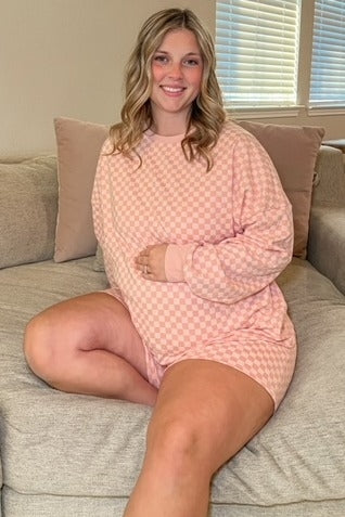 woman wearing a light pink checkered maternity loungewear set, sitting with her baby bump on display
