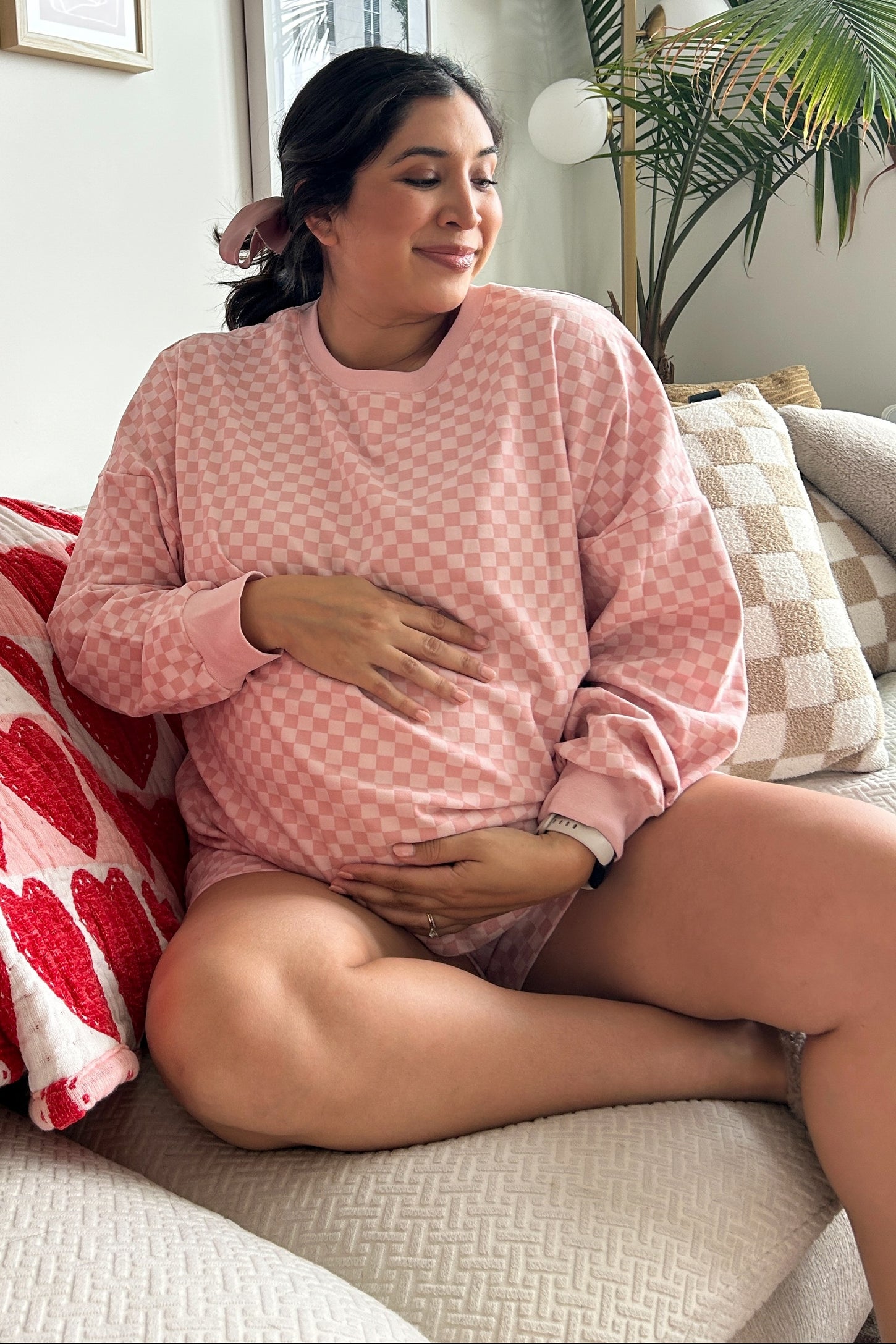 woman wearing a pink checkered maternity sweatshirt and shorts, sitting with a visible baby bump
