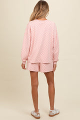woman wearing a pink checkered maternity loungewear set with long sleeves and shorts, showing a relaxed fit