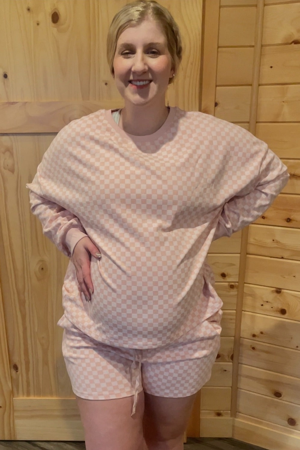 woman wearing a pink checkered maternity lounge set with shorts and a loose-fitting top, highlighting her baby bump