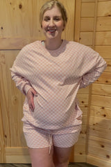 woman wearing a pink checkered maternity lounge set with shorts and a loose-fitting top, highlighting her baby bump