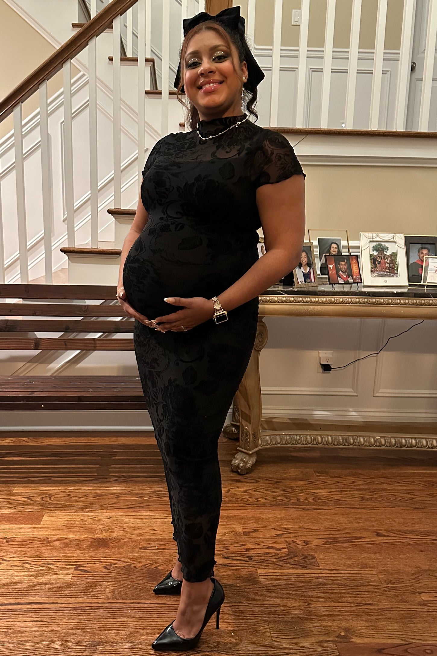 woman wearing a black lace maternity dress and holding her baby bump while standing on a staircase
