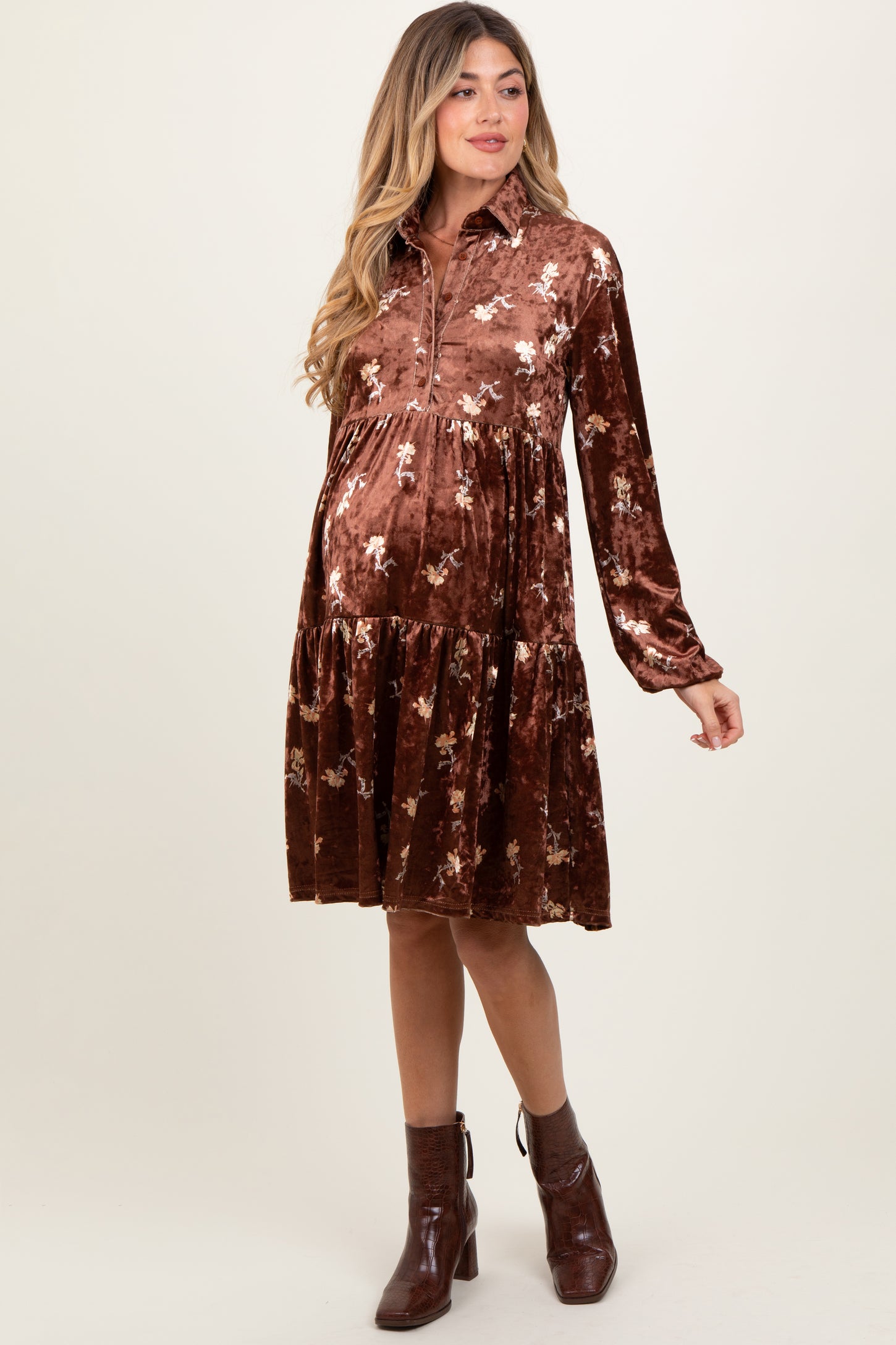 woman wearing a brown velvet maternity dress with floral print and a tiered skirt, showing her baby bump