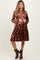 woman wearing a brown velvet floral maternity dress with a collared neckline and tiered skirt, standing confidently
