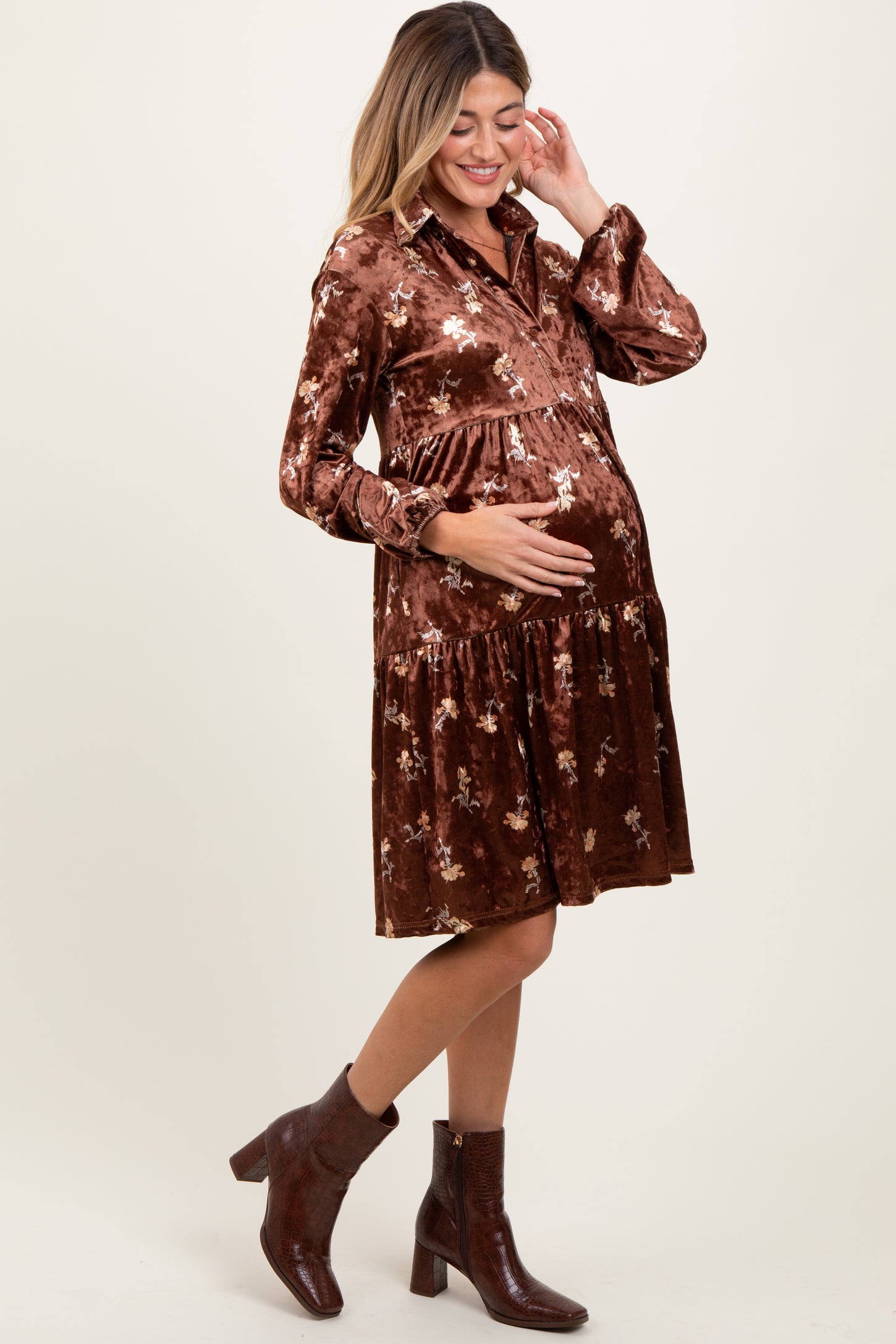 woman wearing a brown floral velvet maternity dress and holding her baby bump