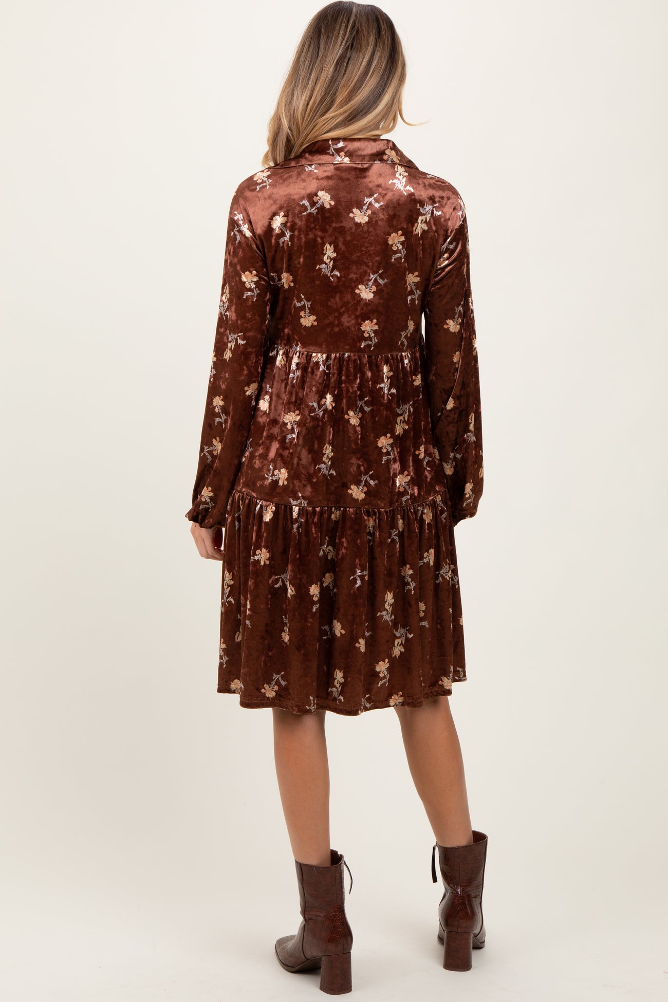 woman wearing a brown floral velvet maternity dress with long sleeves and a tiered skirt, showing her baby bump