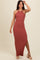 woman wearing a rust ribbed halter neck maxi dress and nude heeled sandals, posing with one hand on her hair