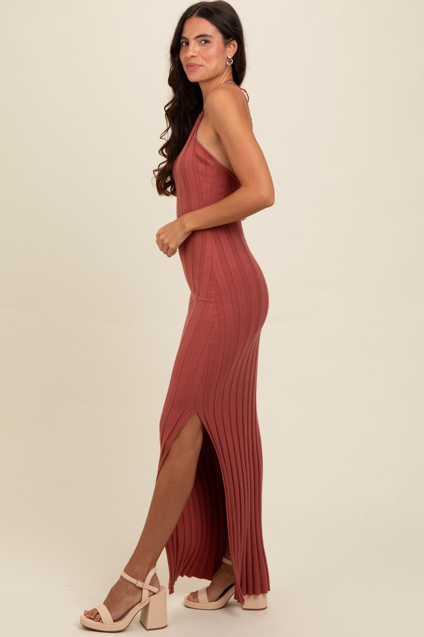 woman wearing a rust-colored ribbed maxi dress with side slits and strappy heels