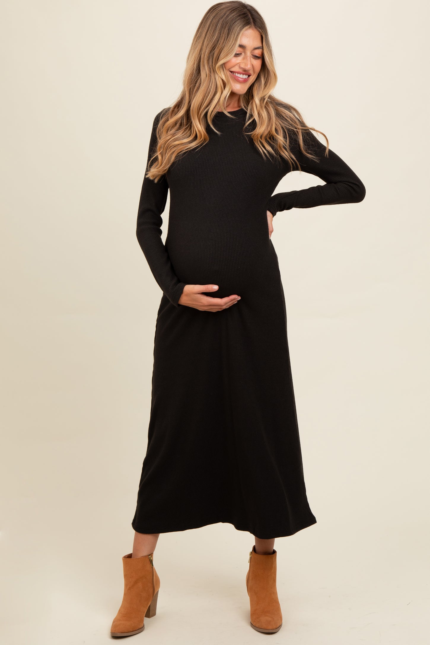 woman wearing a black ribbed maternity maxi dress and holding her baby bump, paired with tan ankle boots