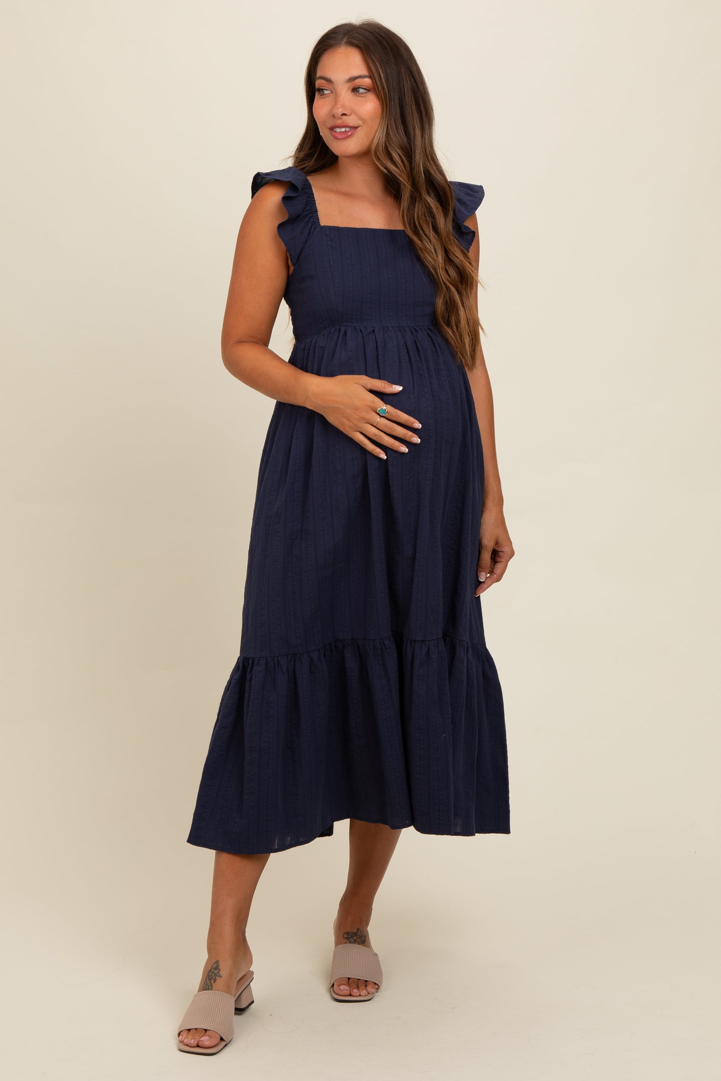 woman wearing a navy blue maternity dress with ruffle sleeves and a tiered skirt, showing her baby bump