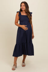 woman wearing a navy blue maternity dress with ruffle sleeves and a tiered skirt, showing her baby bump
