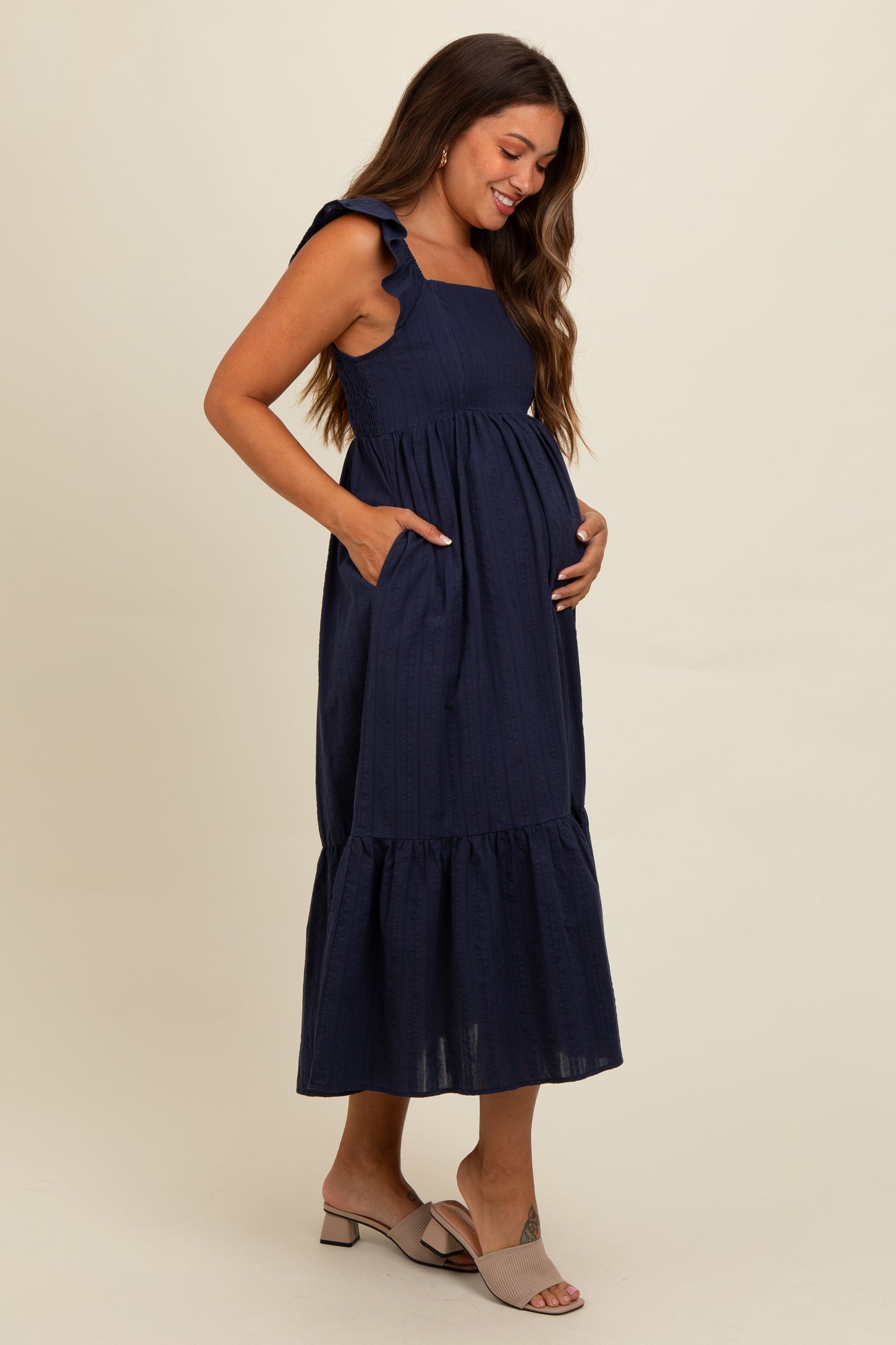 woman wearing a navy blue maternity dress with ruffled straps and a tiered skirt, gently cradling her baby bump