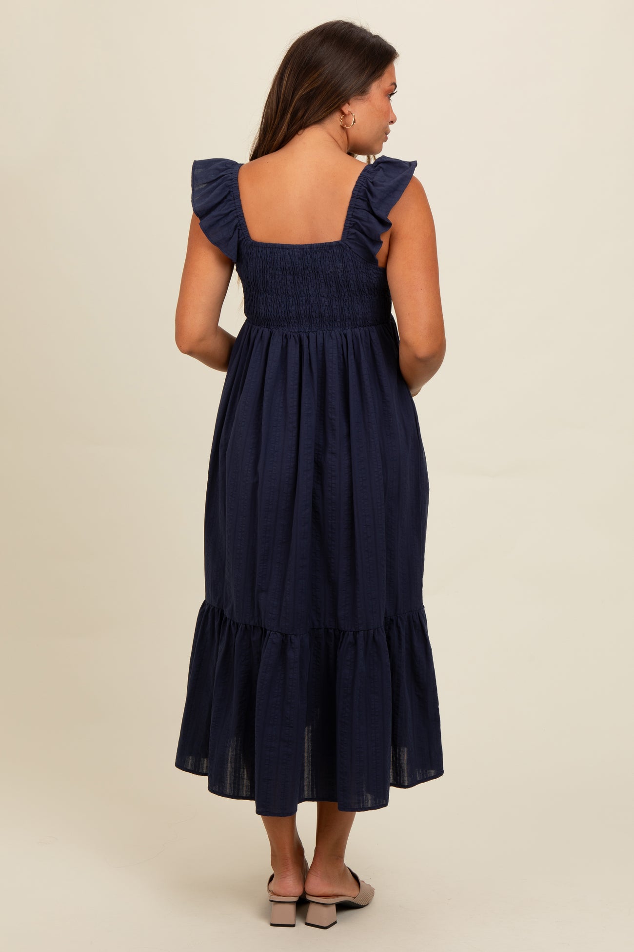 woman wearing a navy blue maternity dress with ruffle sleeves and a tiered skirt, showing her back