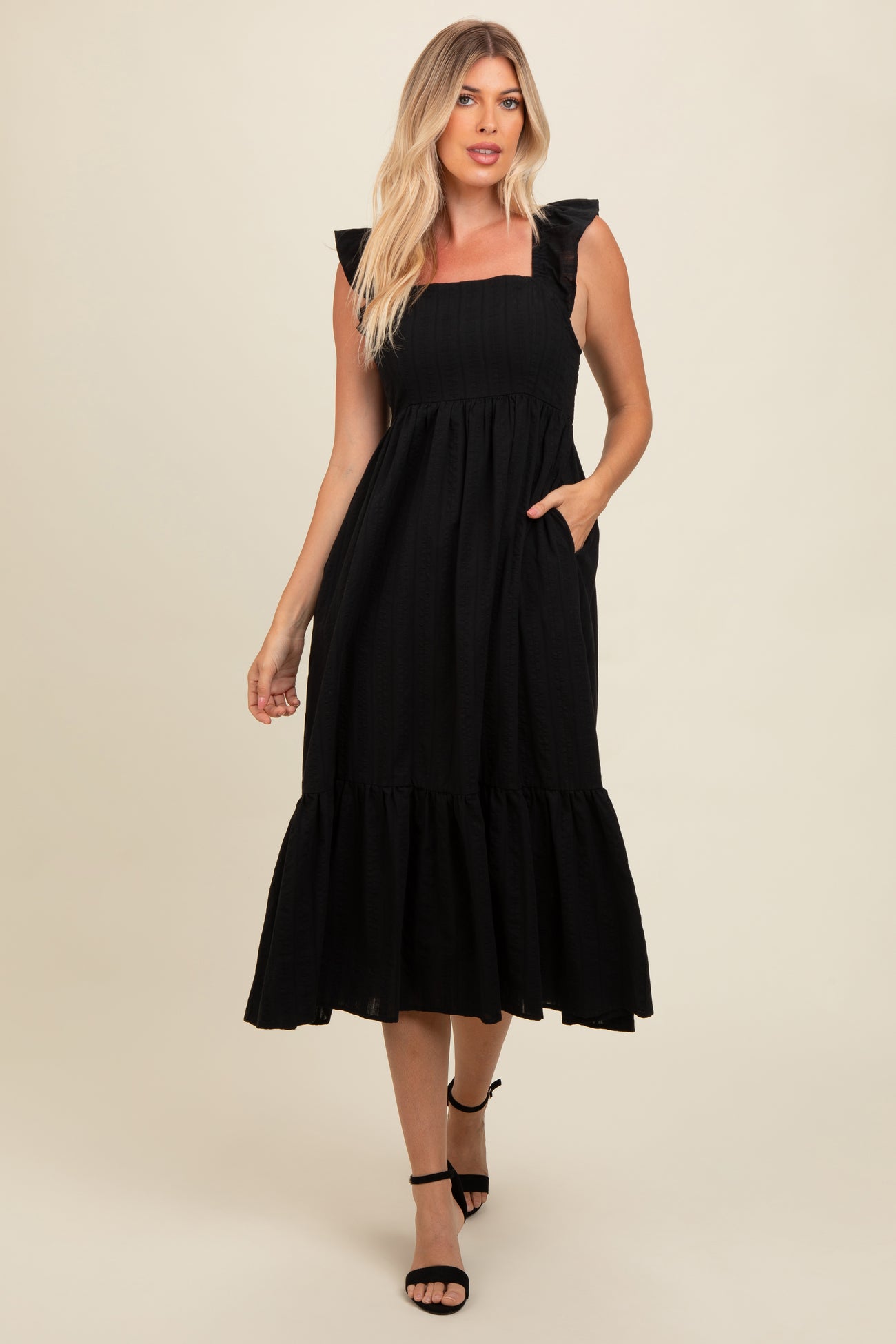 woman wearing a black ruffled sleeve midi dress with a tiered skirt and pockets