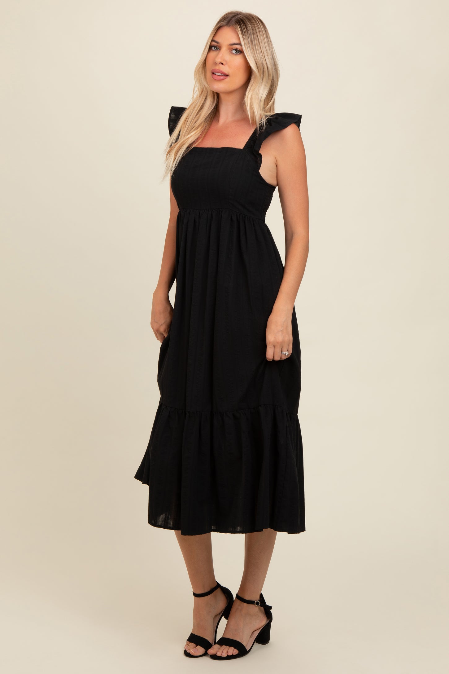woman wearing a black midi dress with ruffled straps and a tiered hem, styled with black heeled sandals