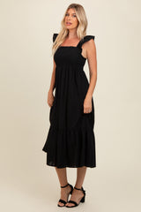 woman wearing a black midi dress with ruffled straps and a tiered hem, styled with black heeled sandals