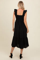 woman wearing a black midi dress with ruffled sleeves and a smocked back design, shown from the back
