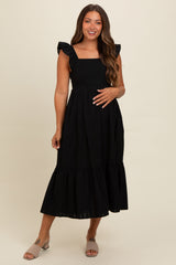 woman wearing a black maternity dress with ruffle straps and a tiered skirt, styled for comfort during pregnancy
