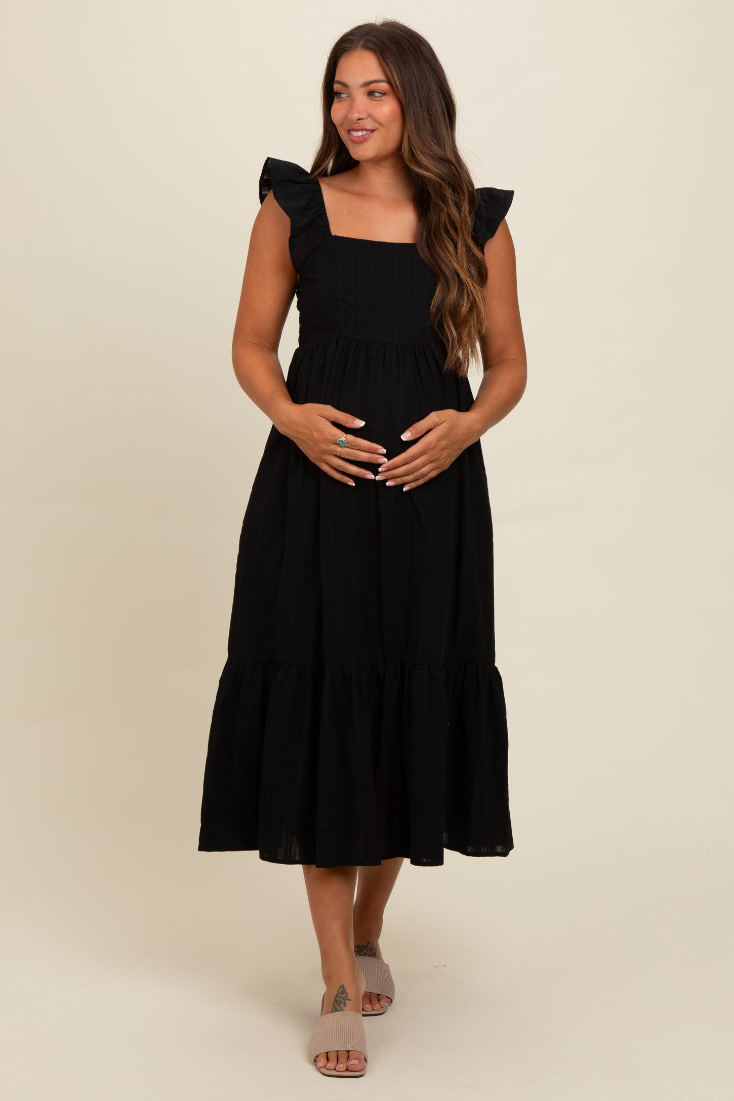 woman wearing a black maternity dress with ruffled sleeves and a tiered skirt, holding her baby bump