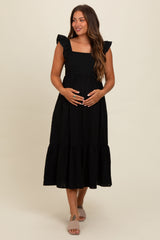 woman wearing a black maternity dress with ruffled sleeves and a tiered skirt, holding her baby bump