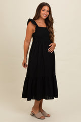 woman wearing a black maternity dress with ruffled straps and a tiered skirt, showing her baby bump