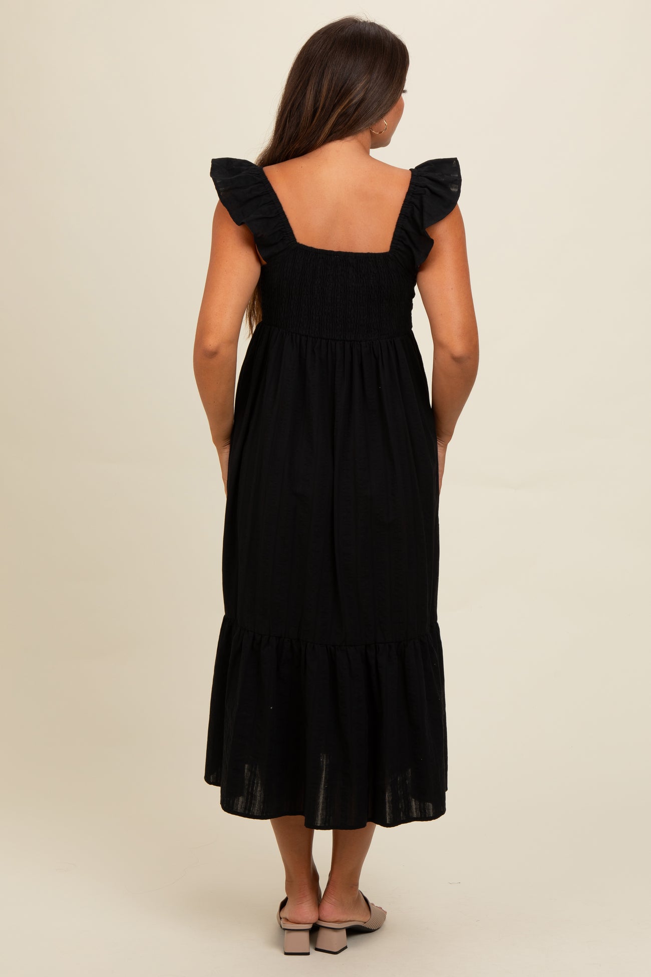 woman wearing a black maternity dress with ruffled straps and a tiered hem, showing a baby bump from the back