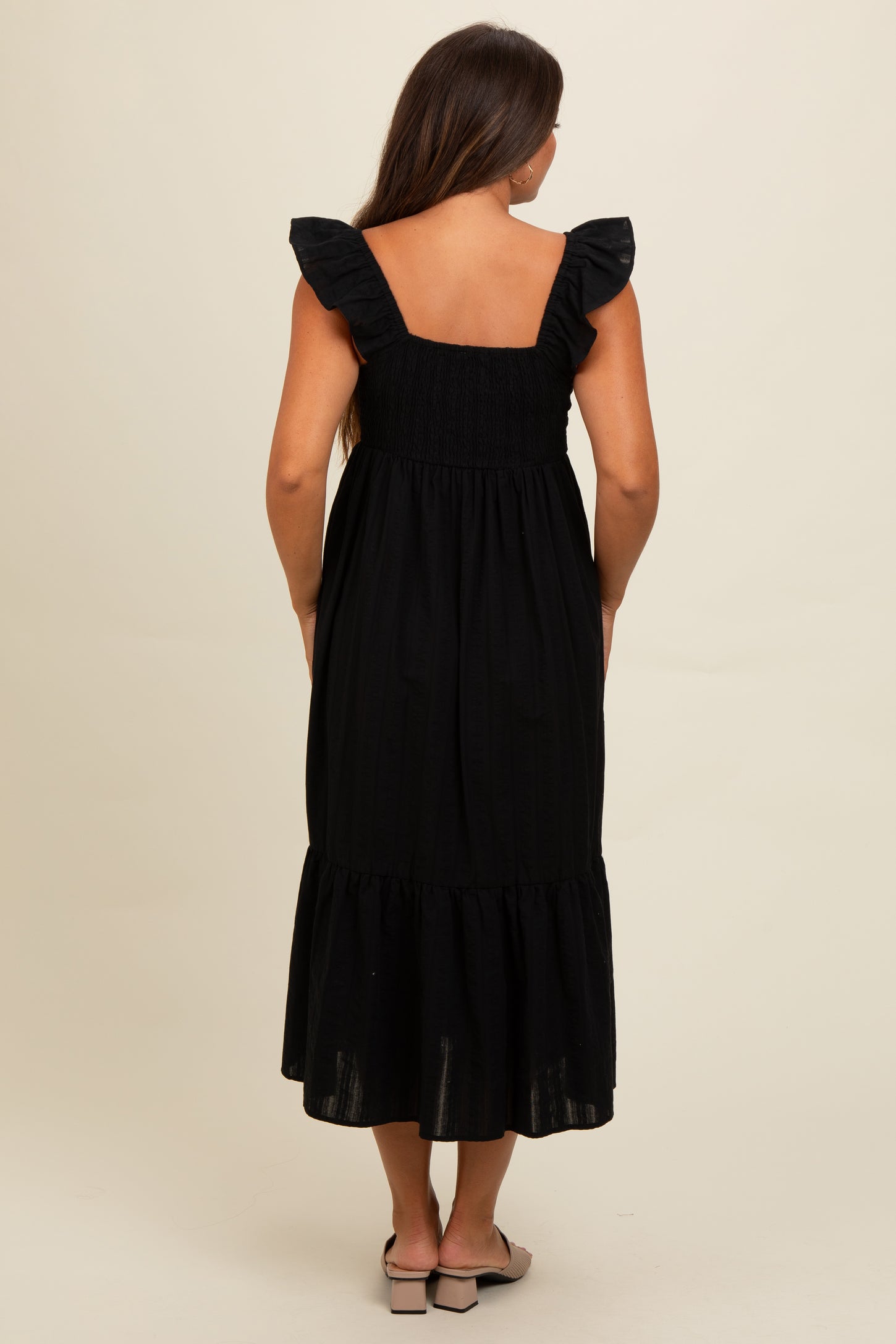 woman wearing a black maternity dress with ruffled straps and a tiered hem, showing a baby bump from the back