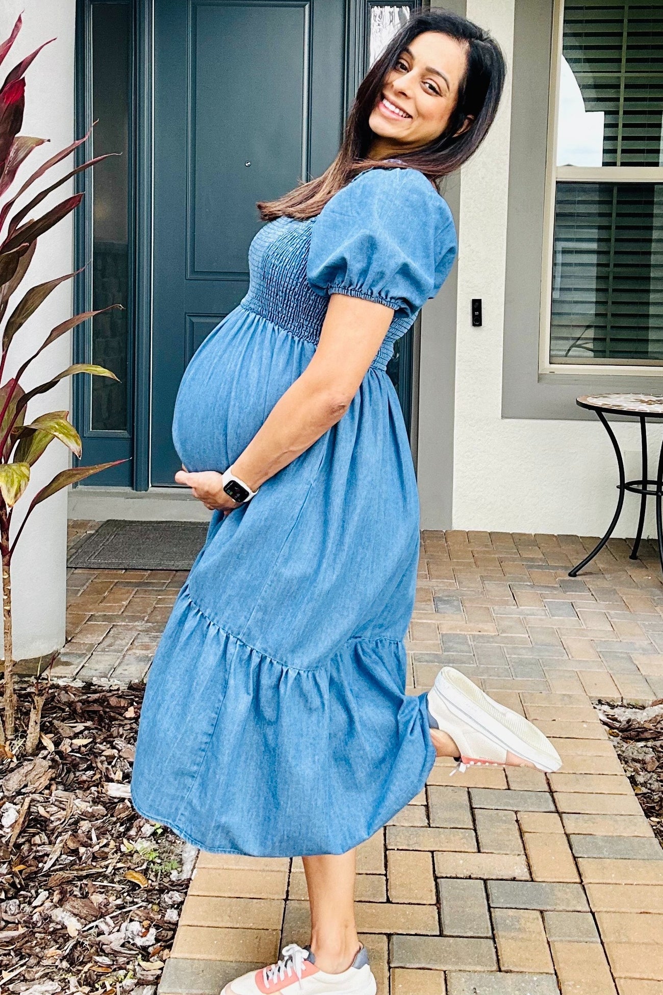 woman wearing a denim maternity dress with puff sleeves and tiered skirt, highlighting her baby bump