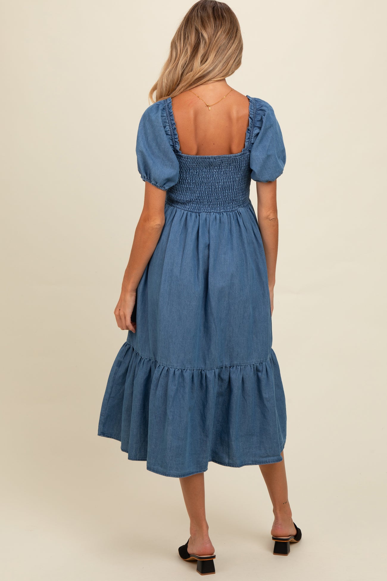 woman wearing a denim maternity dress with puff sleeves and a smocked bodice, showing a flowing skirt from the back