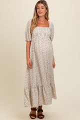 woman wearing a cream floral maternity maxi dress with puff sleeves and a tiered hem, showing her baby bump